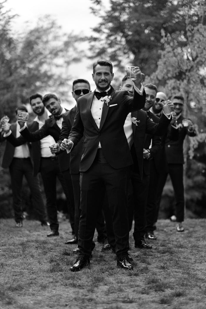 services-02 Stylish groom with groomsmen in tuxedos celebrating outdoors in a black and white photo.
