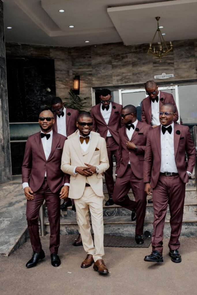 pexels photo 31184294 Stylish groomsmen in matching burgundy suits with the groom in cream, posing confidently outdoors.