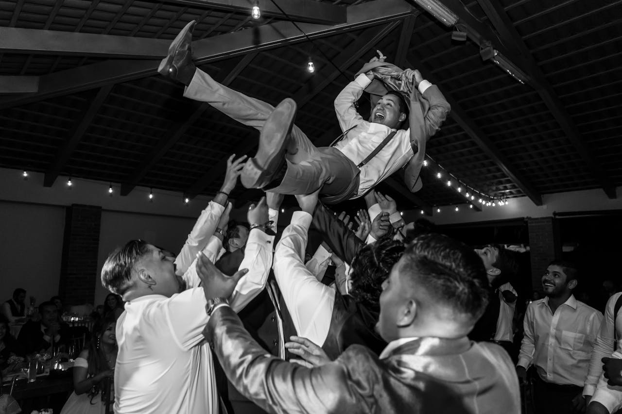gallery-2 A jubilant group of men lifting a friend in celebration during a lively indoor party.